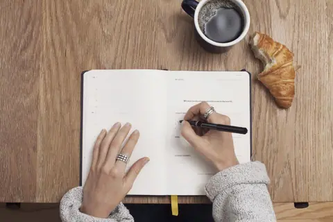 Mani che prendono appunti su un quaderno accanto a una tazza di caffè