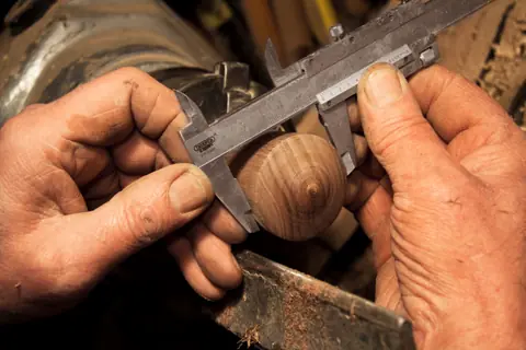 Mani di un artigiano che misura un pezzo di legno con il calibro
