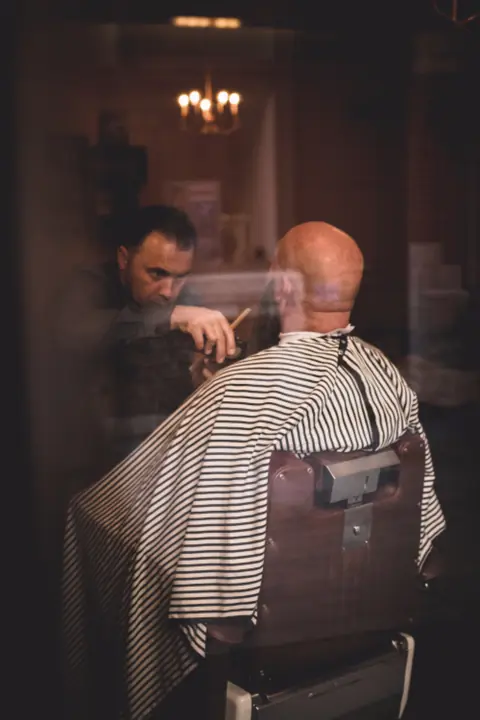 Cliente sulla poltrona del barbiere con mantellina a righe